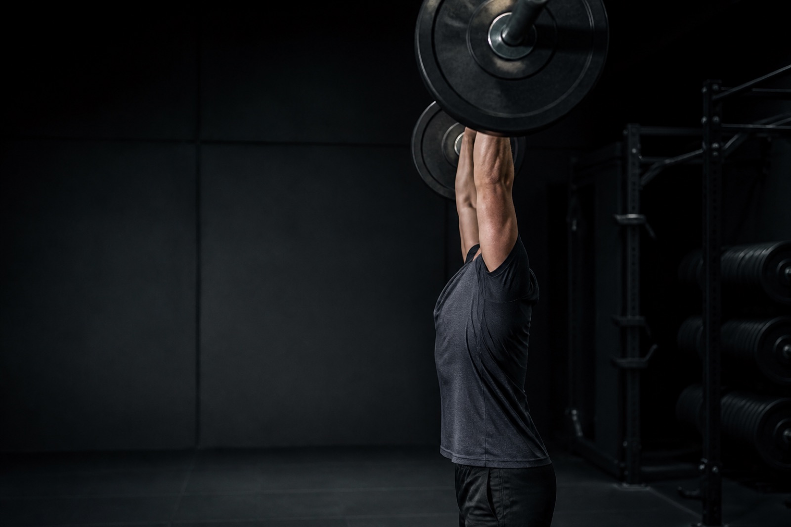 Person som utför militärpress med skivstång i ett gym, sedd från sidan
