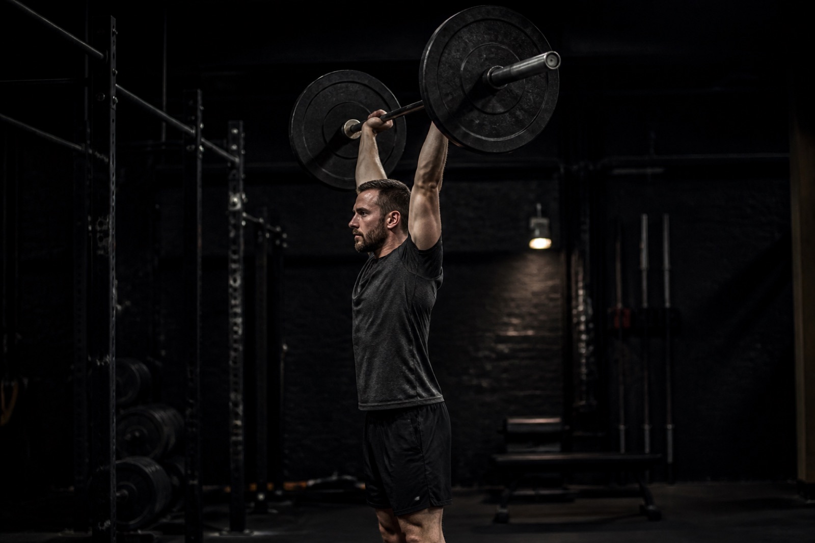 Person som utför stående axelpress med skivstång i ett gym, sedd från sidan