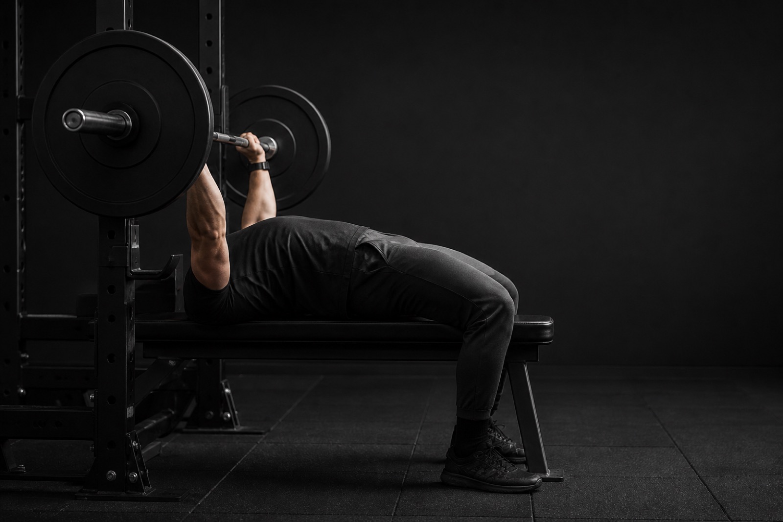 Person som utför bänkpress med skivstång i ett gym, sedd från sidan med skulderbladen ihopdragna