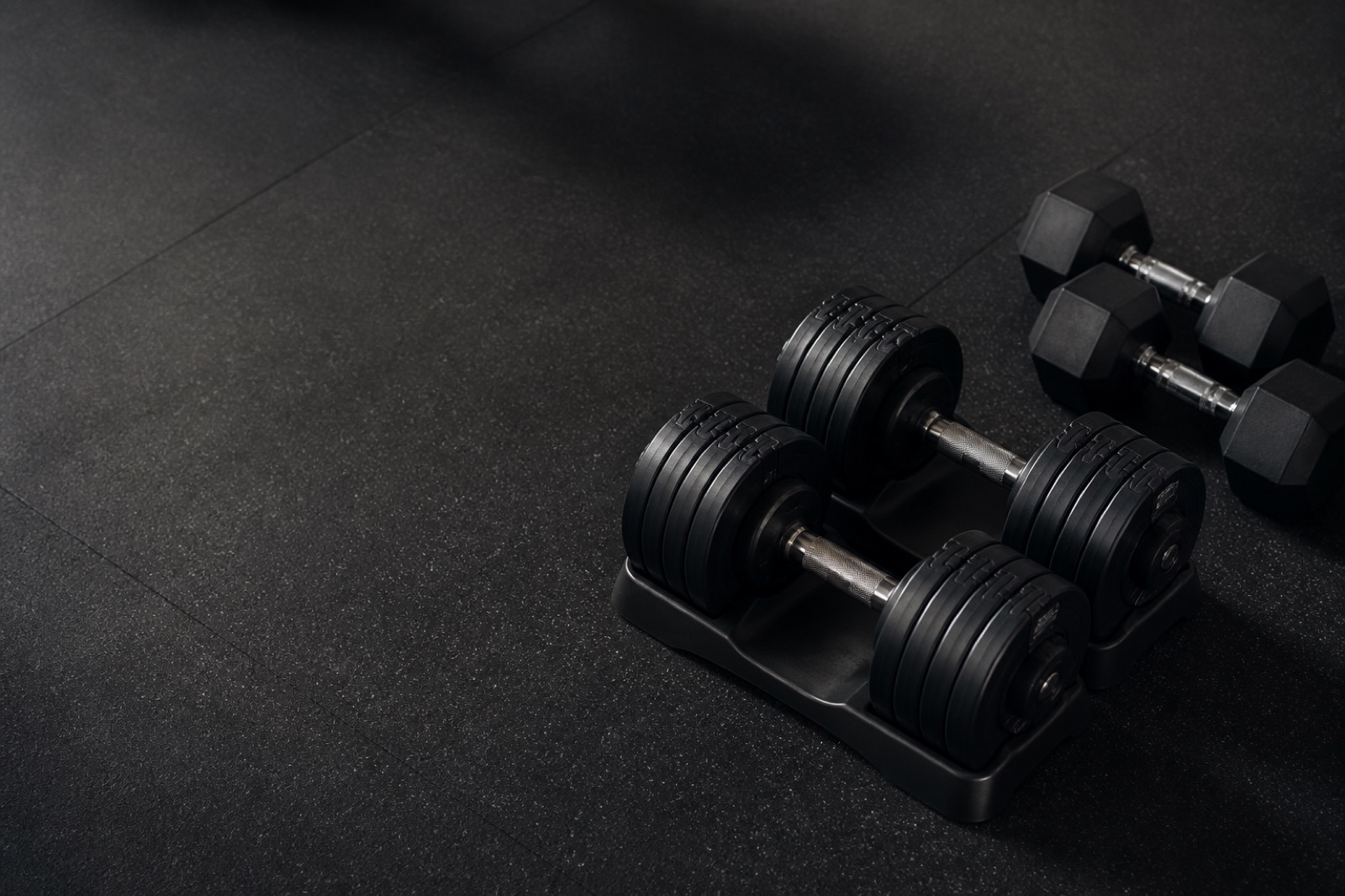 Justerbara hantlar och ett par hexhantlar på ett mörkt gymgolv