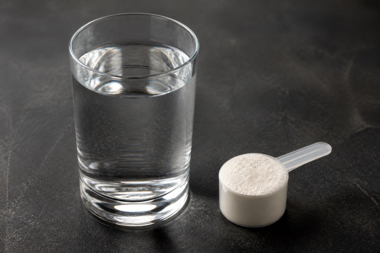 Glas med klar dryck och ett mått elektrolytpulver på en mörk bänkskiva