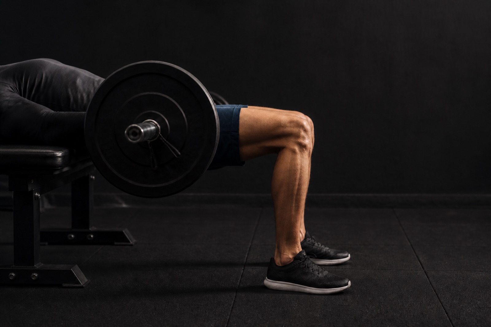 Person som utför hip thrust med skivstång över höften mot en träningsbänk i ett gym