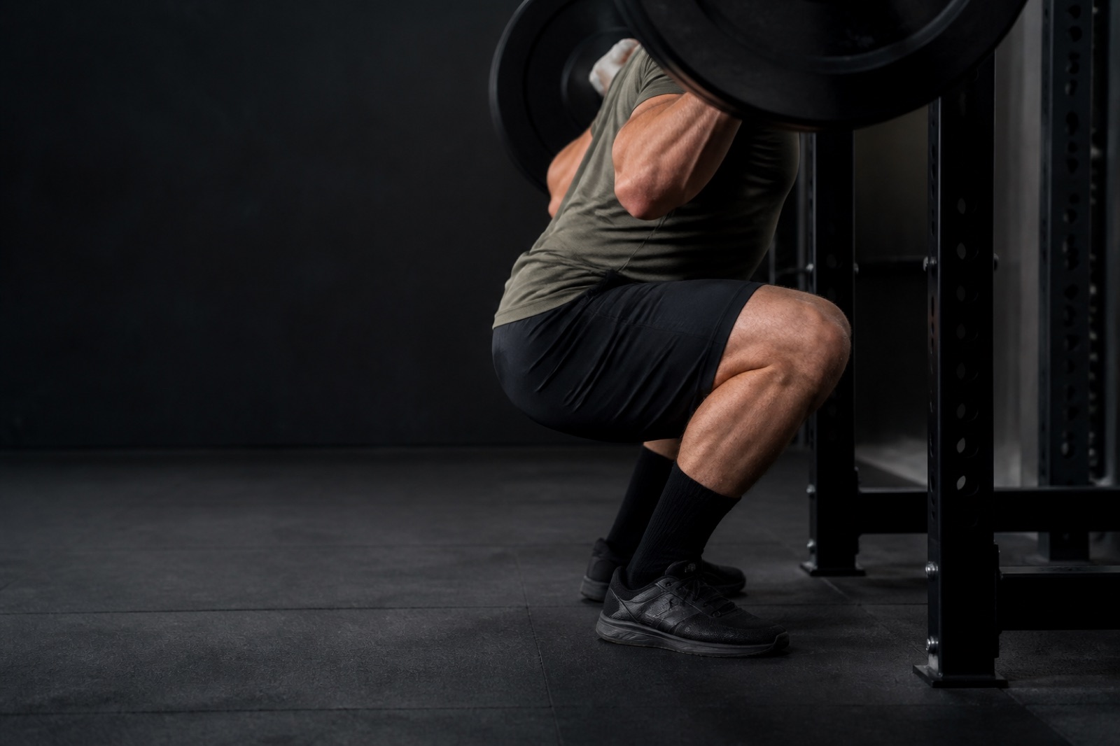 Person som utför knäböj med skivstång på ryggen i ett gym, sedd från sidan i djup position