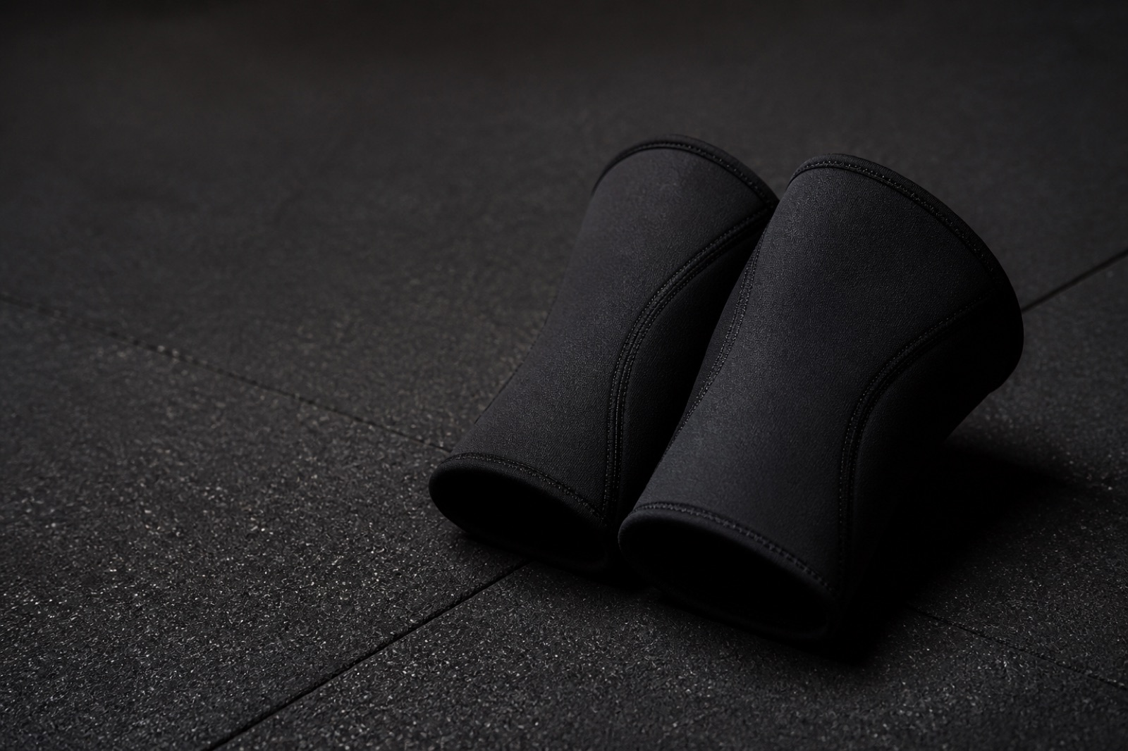 Ett par tjocka svarta knäskydd i neopren på ett mörkt gymgolv