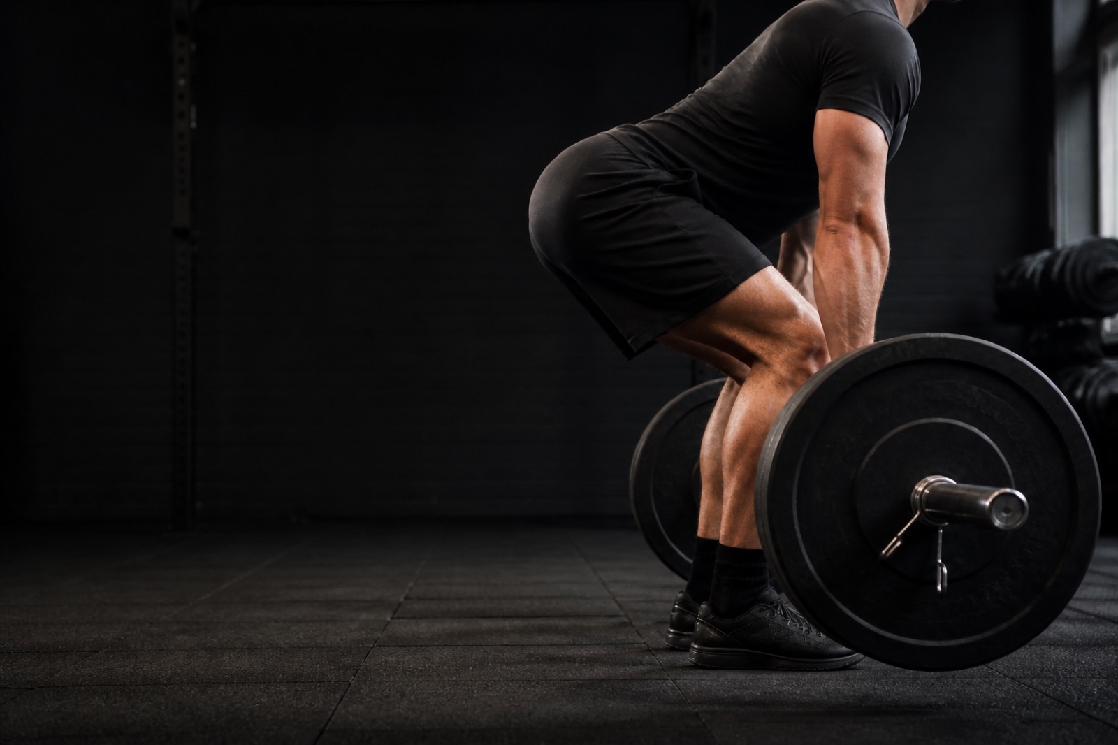 Person som utför marklyft med laddad skivstång i ett gym, sedd från sidan med neutral ryggposition