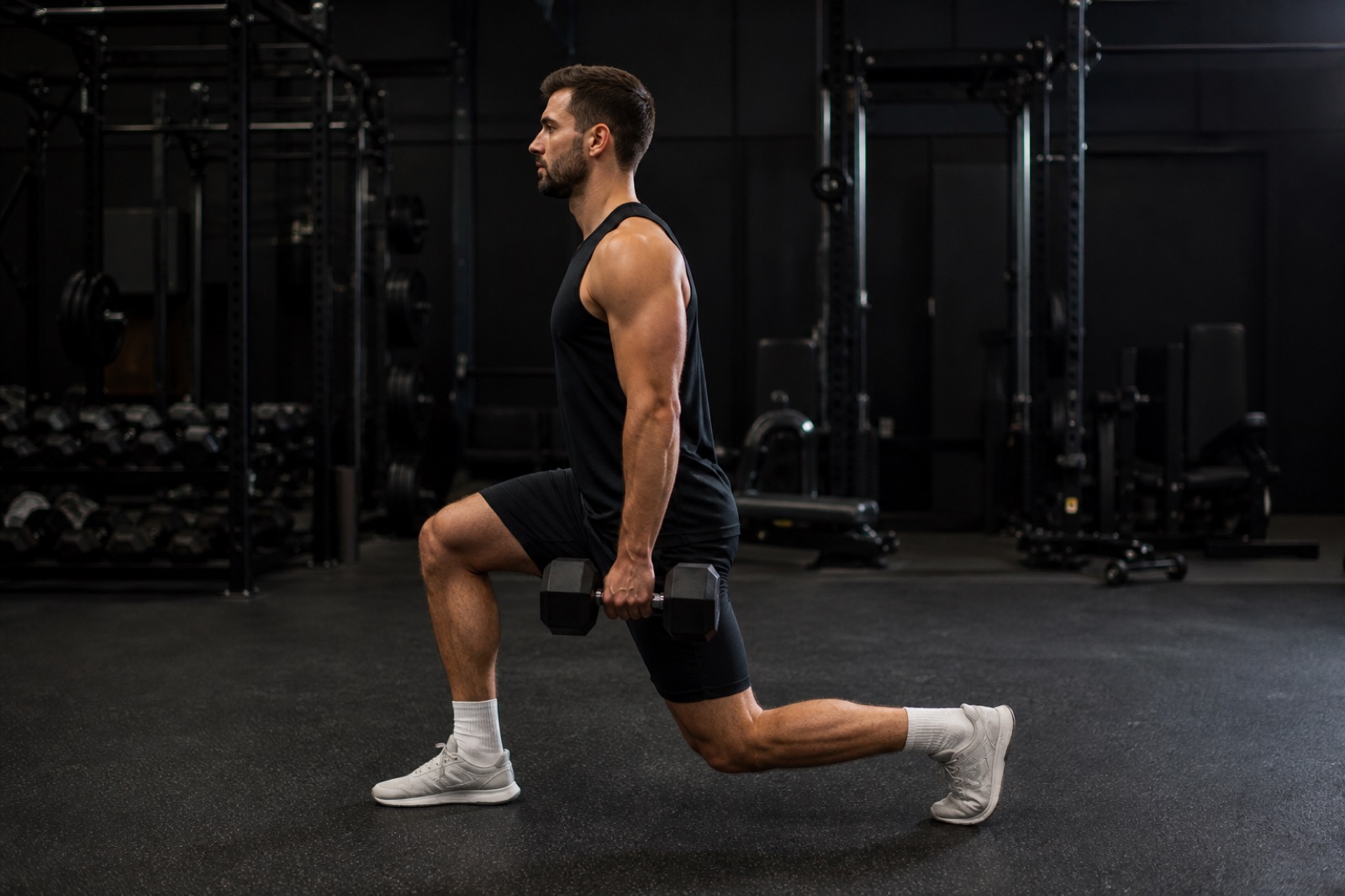 Person som utför utfallssteg med hantlar i ett gym, sedd från sidan