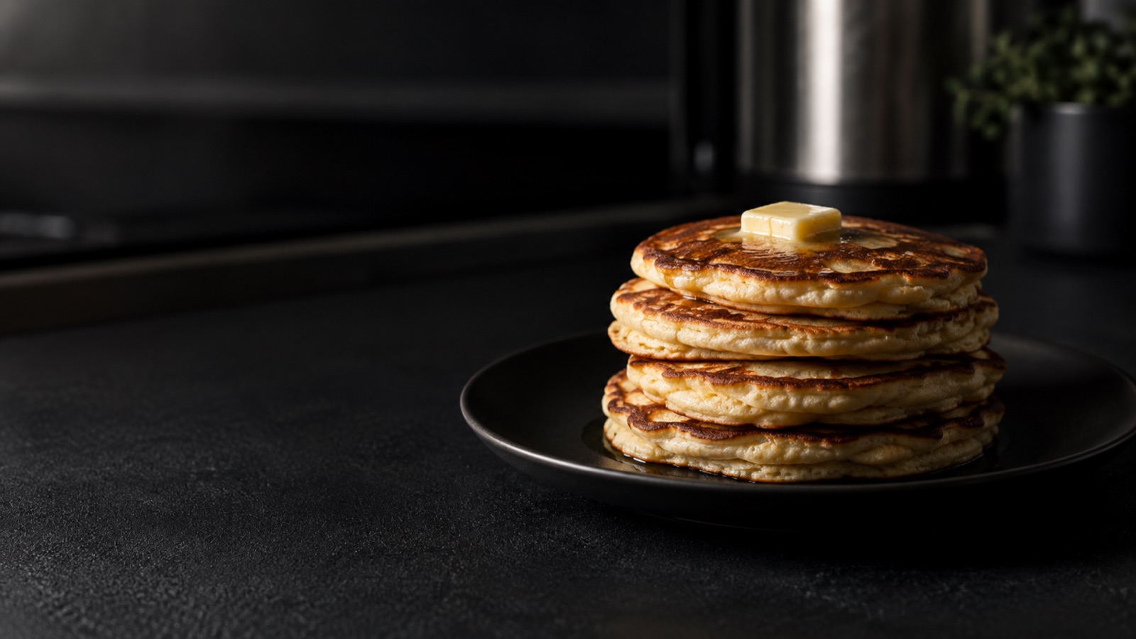 Stapel med proteinpannkakor på en mörk tallrik i ett kök